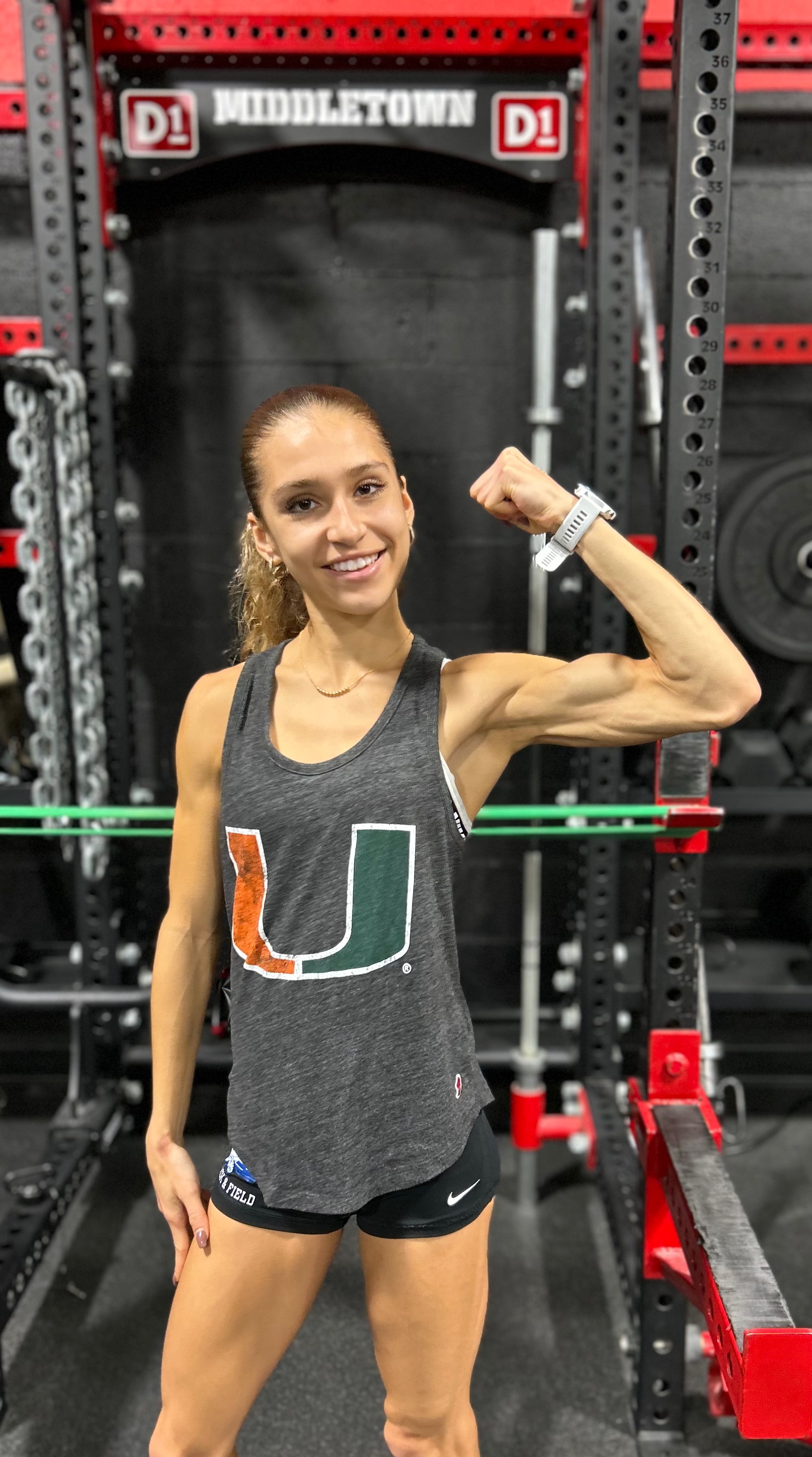 Brielle flexing her arm muscle in a d1 gym