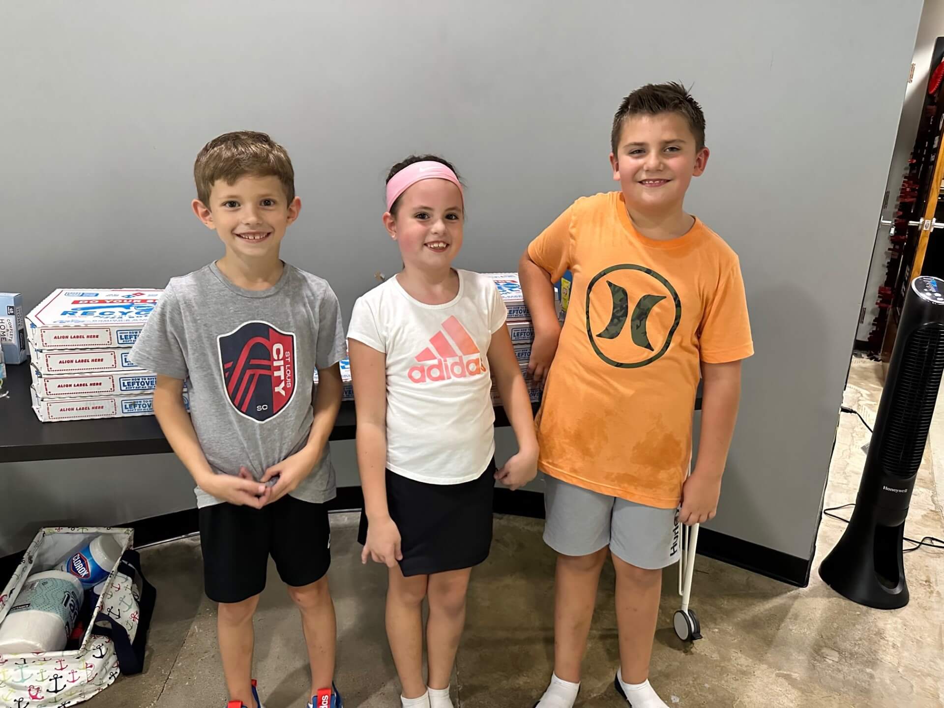 two young boys and a young girl posing in front of a table with pizza at a birthday party at D1 Training St. Louis West