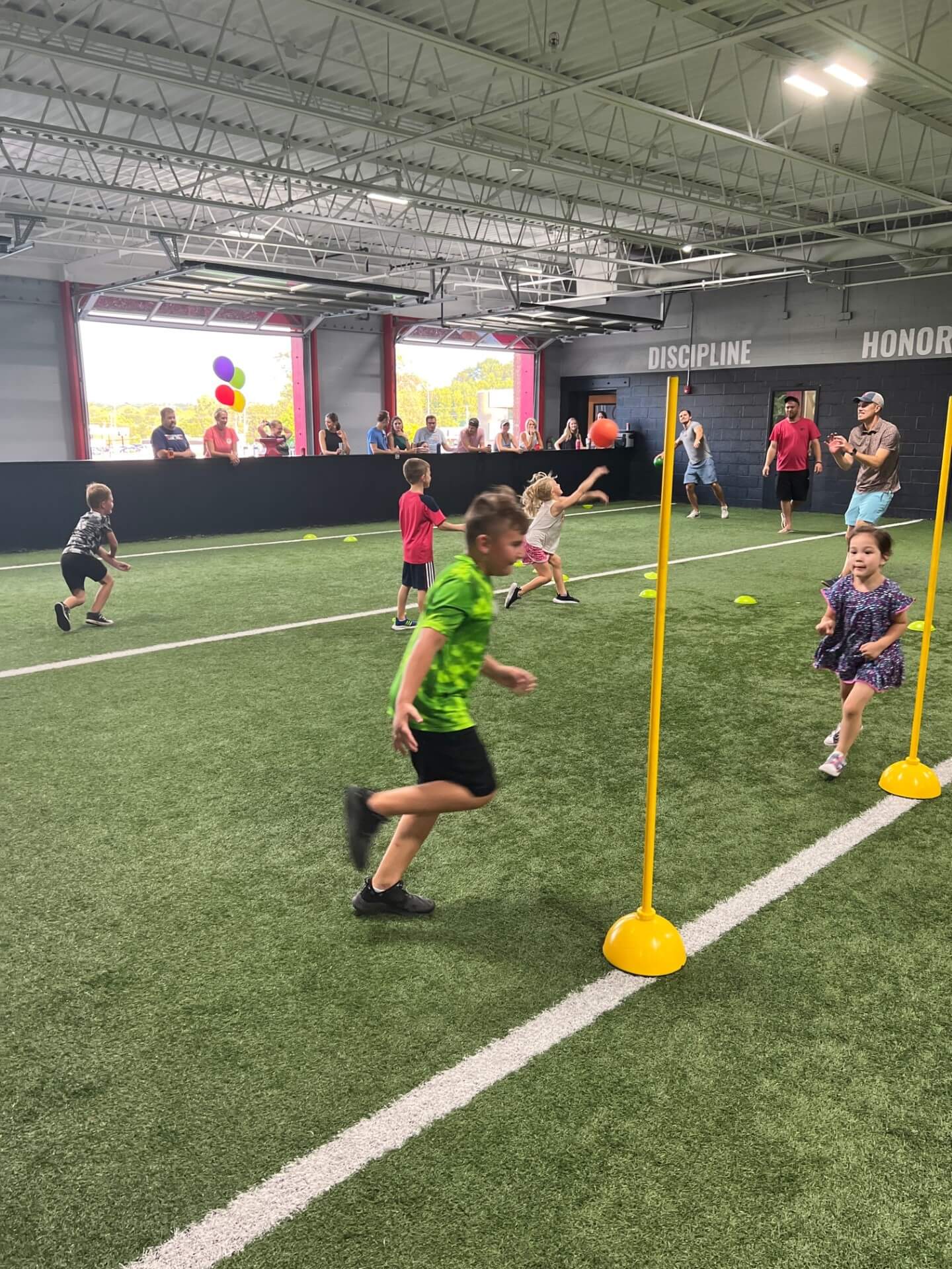 young children playing on the indoor field at D1 Training St. Louis West with their parents watching from the sidelines